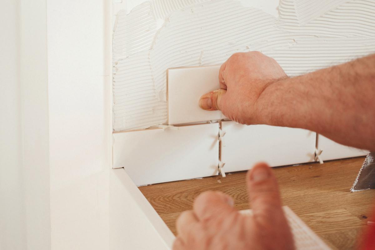 Tiler pressing a white wall tile into adhesive